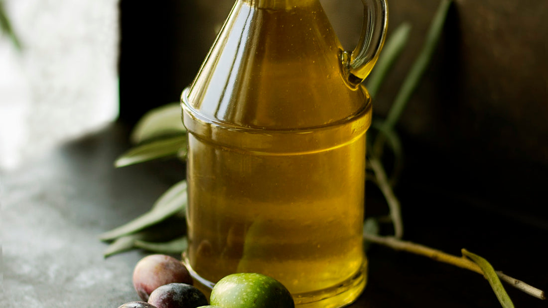 Golden cold-pressed oil in a glass cruet with fresh olives and an olive branch