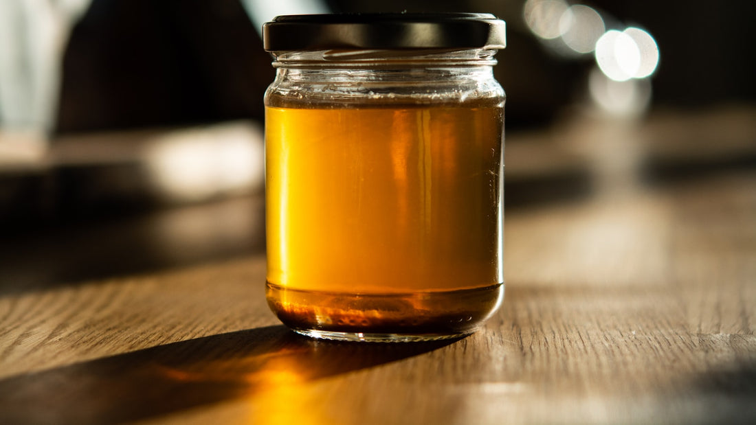 A jar of raw amber honey on a wooden table in warm natural light